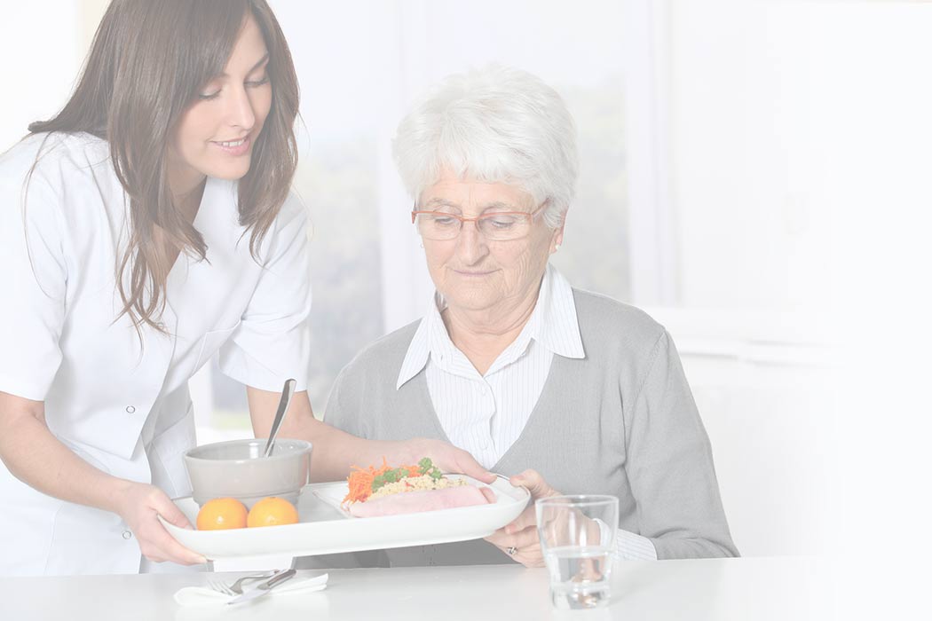 Caregiver serving meal to elderly woman