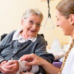 Nurse taking care of senior woman in retirement home bandaging a